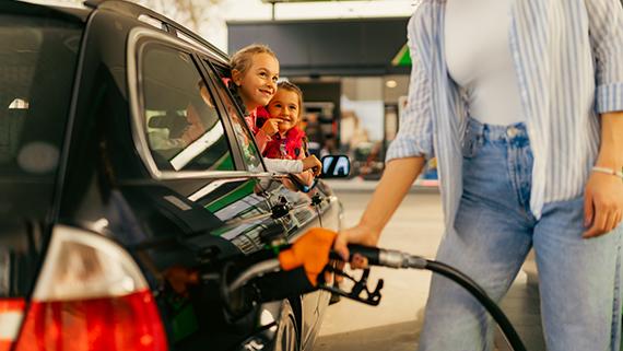Two children watching their mother fill up their car with gas.