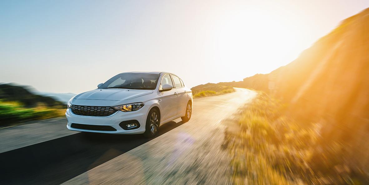White vehicle driving on road next to hill.